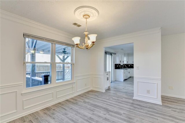 unfurnished dining area with light hardwood / wood-style floors, an inviting chandelier, ornamental molding, and sink