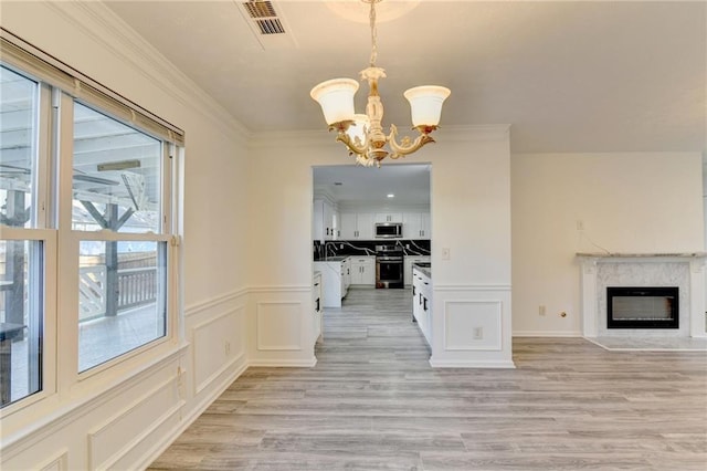 unfurnished dining area featuring a premium fireplace, an inviting chandelier, ornamental molding, and light wood-type flooring