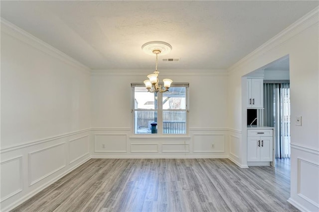 unfurnished dining area with a chandelier, light hardwood / wood-style floors, and crown molding