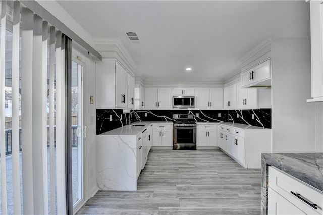 kitchen featuring white cabinetry, backsplash, light stone countertops, and appliances with stainless steel finishes