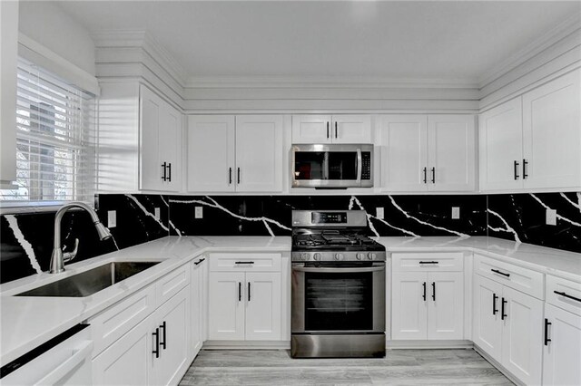 kitchen featuring white cabinetry, sink, light stone counters, decorative backsplash, and appliances with stainless steel finishes