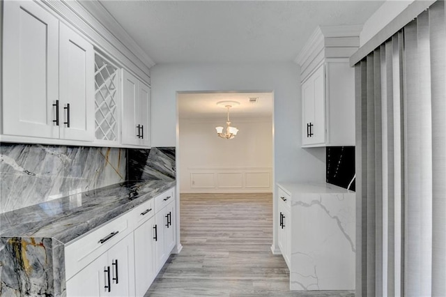 kitchen with light wood-type flooring, backsplash, decorative light fixtures, stone counters, and white cabinetry