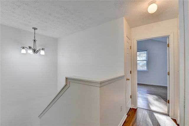 corridor with a textured ceiling, a notable chandelier, and dark wood-type flooring