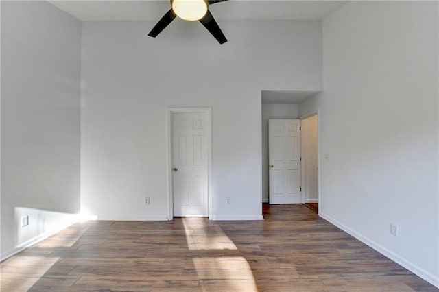 empty room with ceiling fan, dark hardwood / wood-style flooring, and a towering ceiling