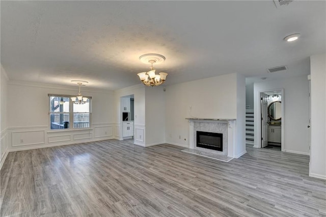 unfurnished living room with crown molding, light hardwood / wood-style flooring, a high end fireplace, and a chandelier