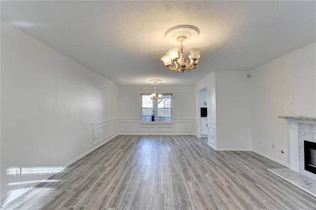 unfurnished living room featuring ornamental molding, a textured ceiling, light wood-type flooring, a fireplace, and a chandelier