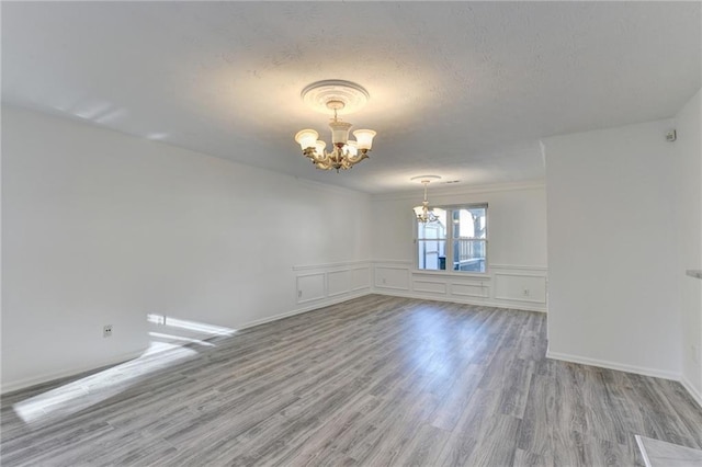 spare room with a textured ceiling, light hardwood / wood-style floors, an inviting chandelier, and ornamental molding