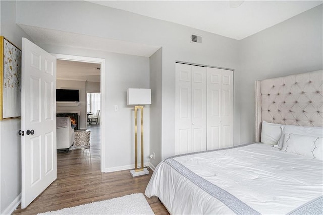 bedroom with wood finished floors, baseboards, a closet, and a lit fireplace