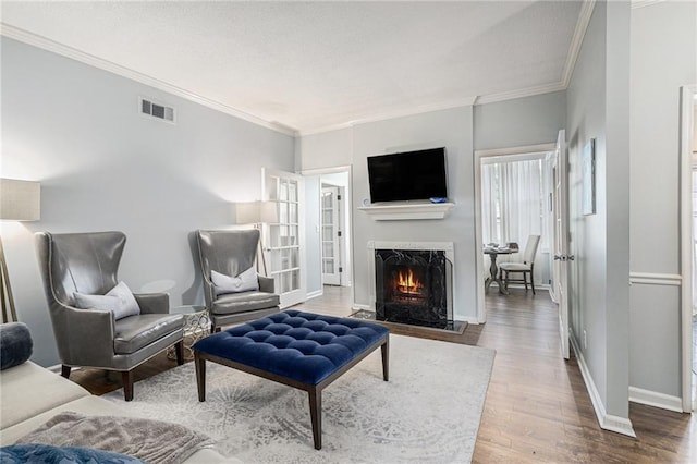 living area featuring a warm lit fireplace, wood finished floors, crown molding, and baseboards