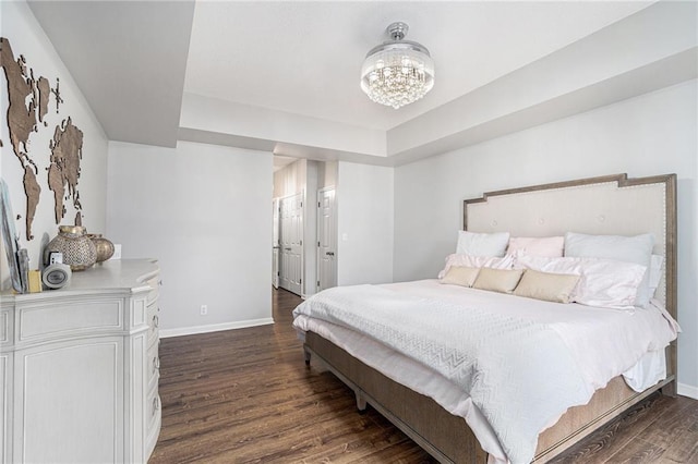 bedroom with baseboards, dark wood-style floors, a tray ceiling, and a chandelier