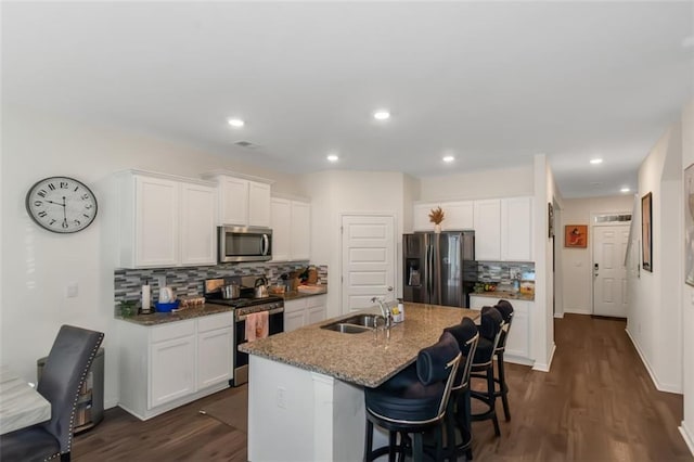 kitchen with a sink, a kitchen island with sink, stainless steel appliances, backsplash, and a breakfast bar area