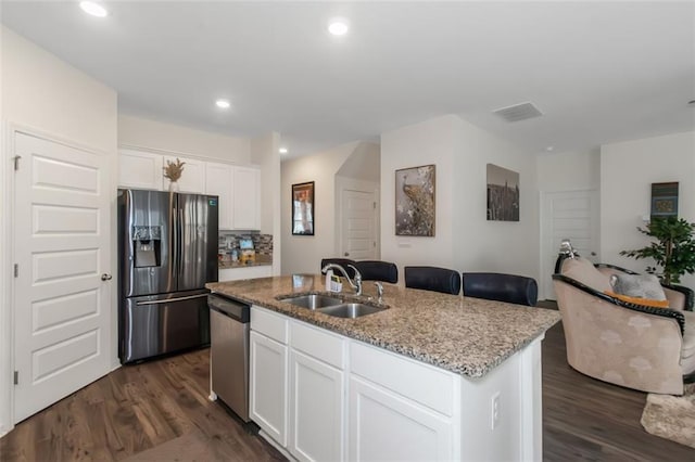 kitchen featuring light stone countertops, a center island with sink, refrigerator with ice dispenser, dishwasher, and a sink