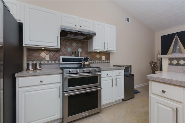 kitchen featuring double oven range, freestanding refrigerator, decorative backsplash, vaulted ceiling, and under cabinet range hood