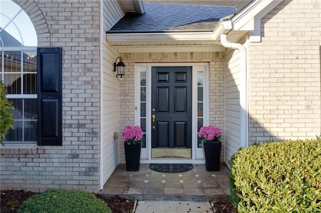 property entrance featuring brick siding and roof with shingles