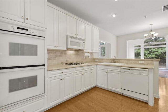 kitchen featuring a peninsula, white appliances, light countertops, a sink, and light wood-style flooring