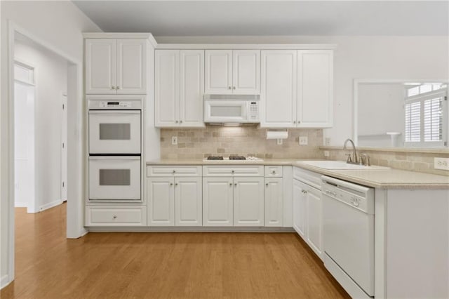 kitchen with a sink, light countertops, white cabinets, white appliances, and light wood-style flooring