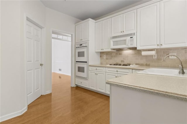 kitchen featuring white cabinets, a sink, white appliances, light wood-style flooring, and backsplash