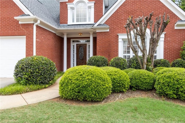 property entrance with brick siding, a shingled roof, and an attached garage