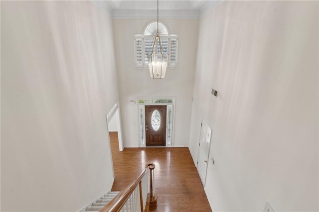 entryway featuring an inviting chandelier, stairs, wood finished floors, a towering ceiling, and ornamental molding