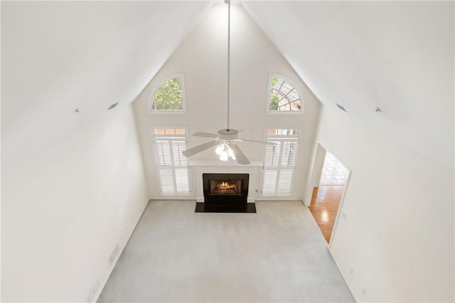 unfurnished living room featuring carpet floors, a fireplace with flush hearth, ceiling fan, and high vaulted ceiling