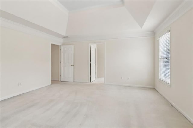 empty room featuring a tray ceiling, light colored carpet, ornamental molding, and baseboards