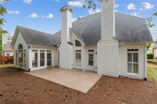 back of house featuring a sunroom, a patio, a chimney, and roof with shingles