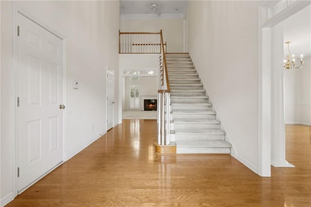 foyer entrance with crown molding, a high ceiling, a chandelier, stairs, and wood finished floors
