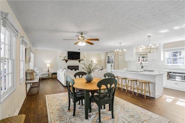 dining area featuring dark hardwood / wood-style floors, a fireplace, ceiling fan with notable chandelier, and a textured ceiling