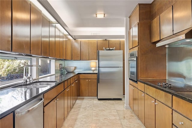 kitchen featuring appliances with stainless steel finishes, dark stone countertops, a sink, under cabinet range hood, and backsplash