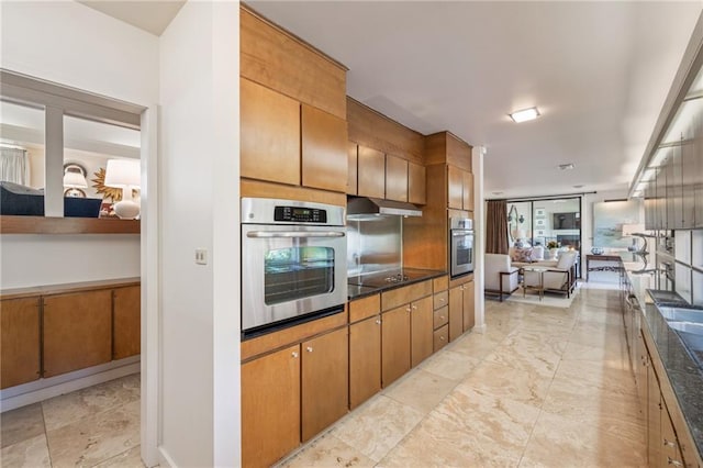 kitchen with brown cabinetry, dark countertops, black electric stovetop, under cabinet range hood, and stainless steel oven