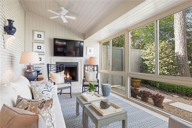 sunroom with lofted ceiling, a lit fireplace, wood ceiling, and a ceiling fan