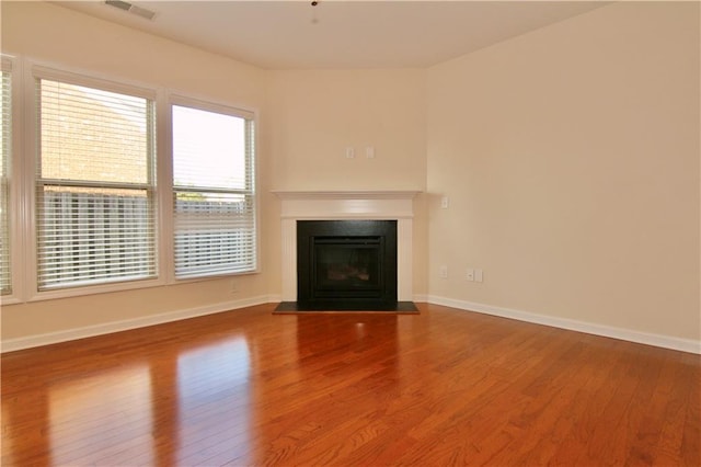 unfurnished living room featuring a fireplace with flush hearth, visible vents, baseboards, and wood finished floors