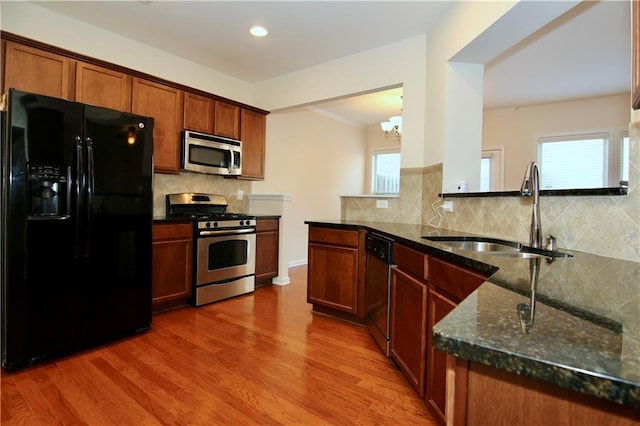 kitchen featuring tasteful backsplash, dark stone counters, wood finished floors, stainless steel appliances, and a sink