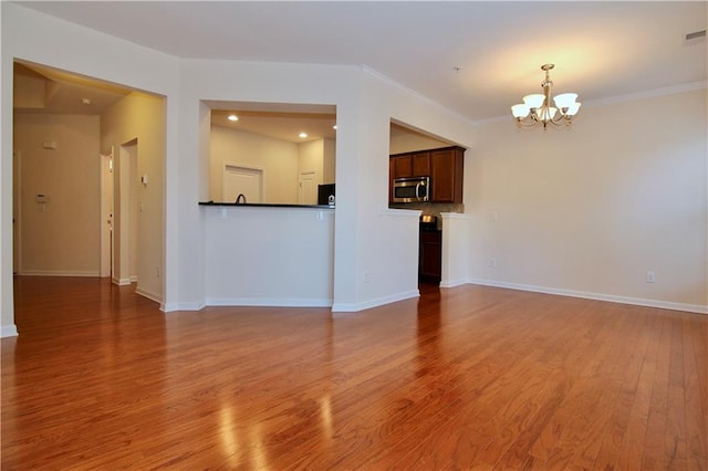 unfurnished living room featuring an inviting chandelier, crown molding, baseboards, and light wood-type flooring