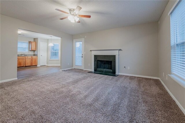 unfurnished living room with a textured ceiling, dark carpet, ceiling fan, and sink