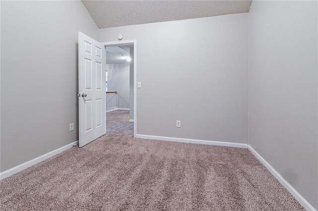 spare room featuring carpet floors, a textured ceiling, and vaulted ceiling