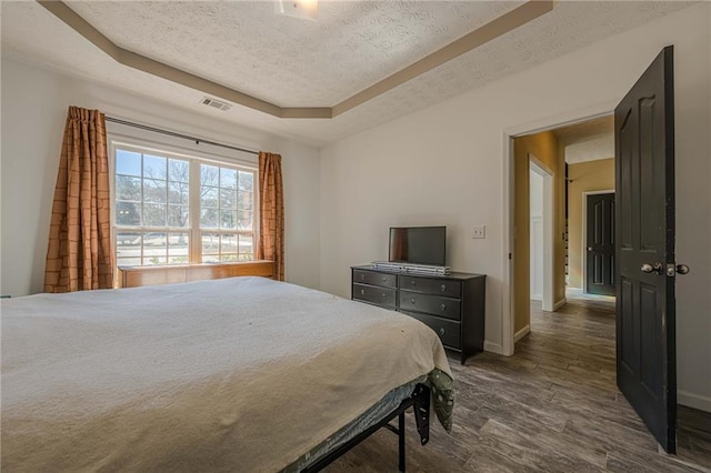 bedroom featuring a textured ceiling, visible vents, baseboards, a tray ceiling, and dark wood finished floors