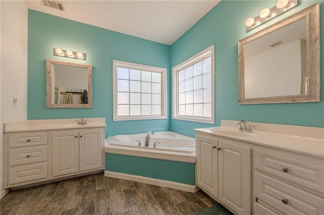 full bathroom featuring two vanities, visible vents, a sink, and a garden tub