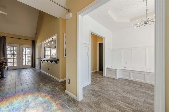 interior space with french doors, a notable chandelier, a raised ceiling, a decorative wall, and wood finished floors