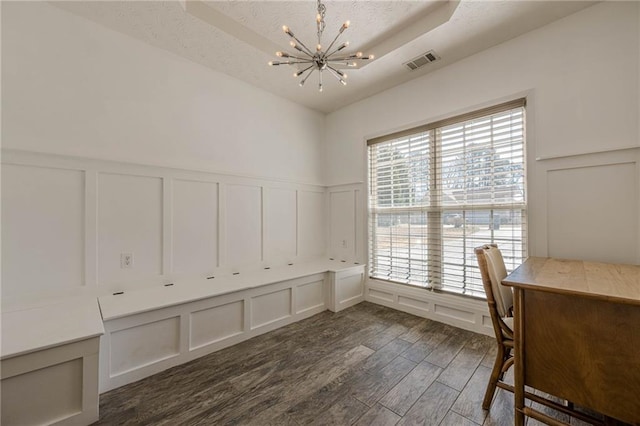 unfurnished office featuring visible vents, dark wood-style floors, an inviting chandelier, a tray ceiling, and a decorative wall