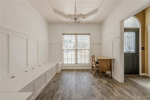 interior space featuring a raised ceiling, dark wood-type flooring, a textured ceiling, a decorative wall, and a notable chandelier