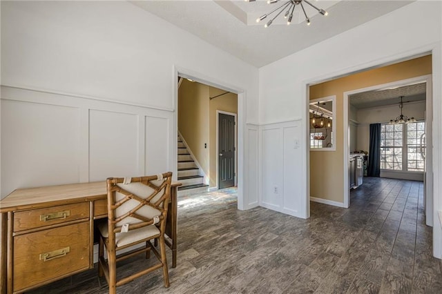 home office featuring a wainscoted wall, dark wood-type flooring, a decorative wall, and a notable chandelier