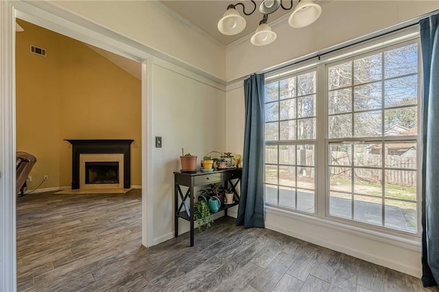 interior space with visible vents, baseboards, a fireplace with flush hearth, wood finished floors, and an inviting chandelier