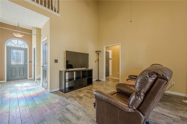 living area featuring a towering ceiling, baseboards, and wood finished floors