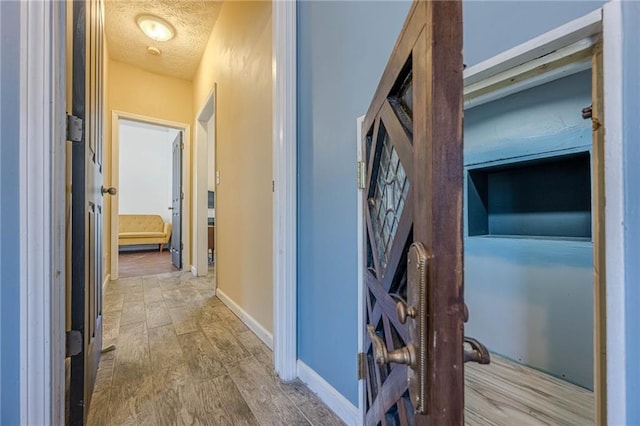 corridor with a textured ceiling, baseboards, and wood finished floors