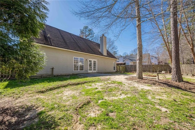 rear view of property featuring a chimney, fence, a lawn, and french doors