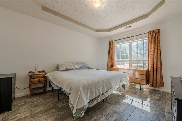 bedroom with a raised ceiling, visible vents, dark wood finished floors, and a textured ceiling