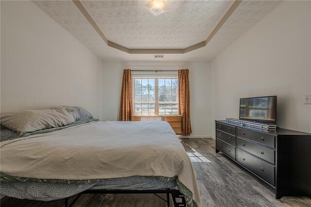 bedroom with baseboards, visible vents, dark wood finished floors, a tray ceiling, and a textured ceiling