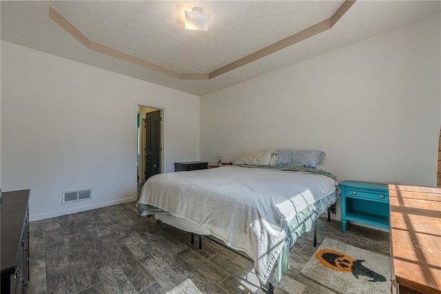 bedroom featuring baseboards, visible vents, a raised ceiling, and wood finished floors