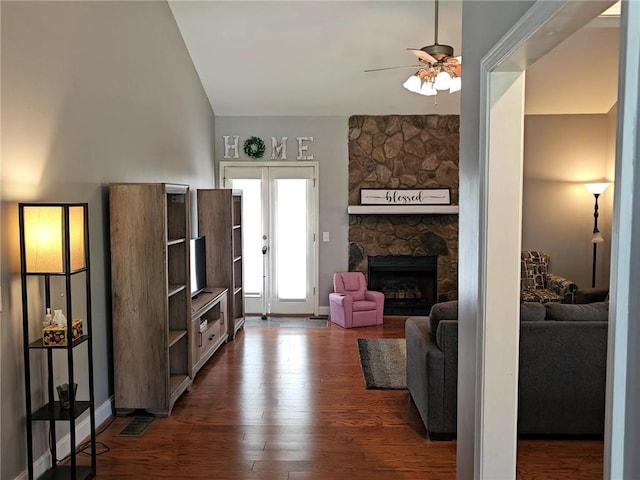 living area with ceiling fan, dark wood finished floors, and a stone fireplace